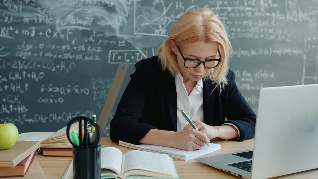 A faculty member working at a desk in front of a chalkboard