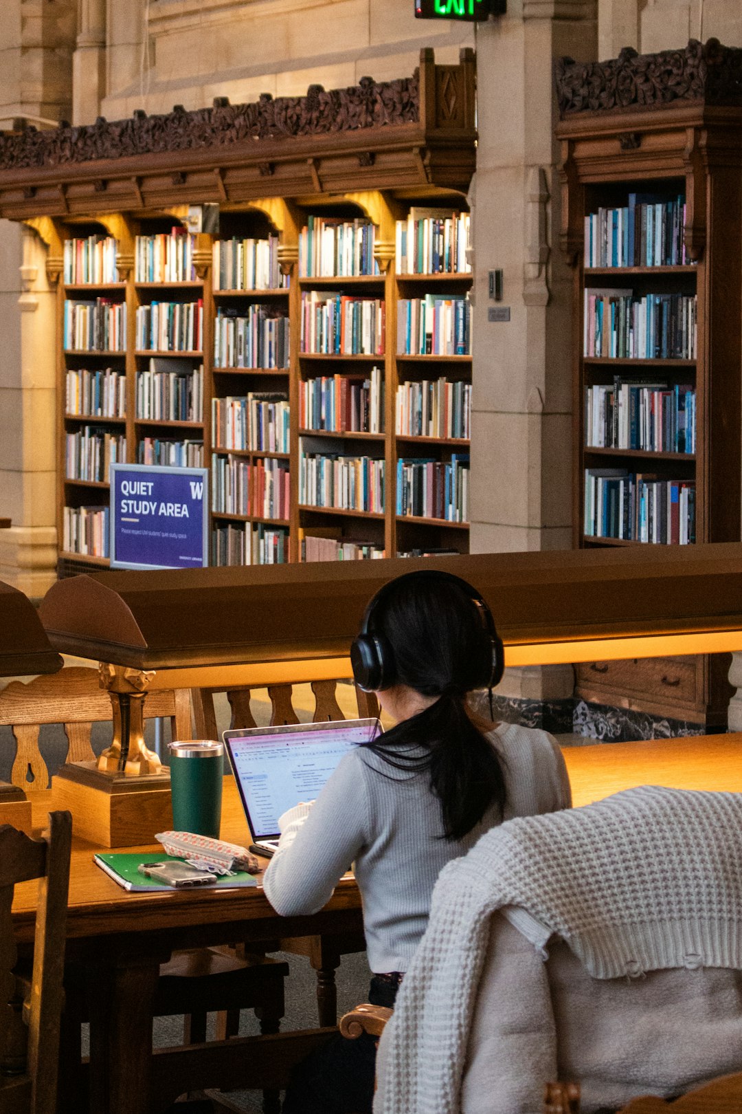 A student studying at a laptop in a university library reading room