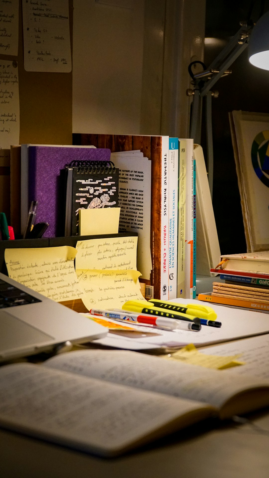 A study desk with an open book, laptop, handwritten notes, and highlighted documents