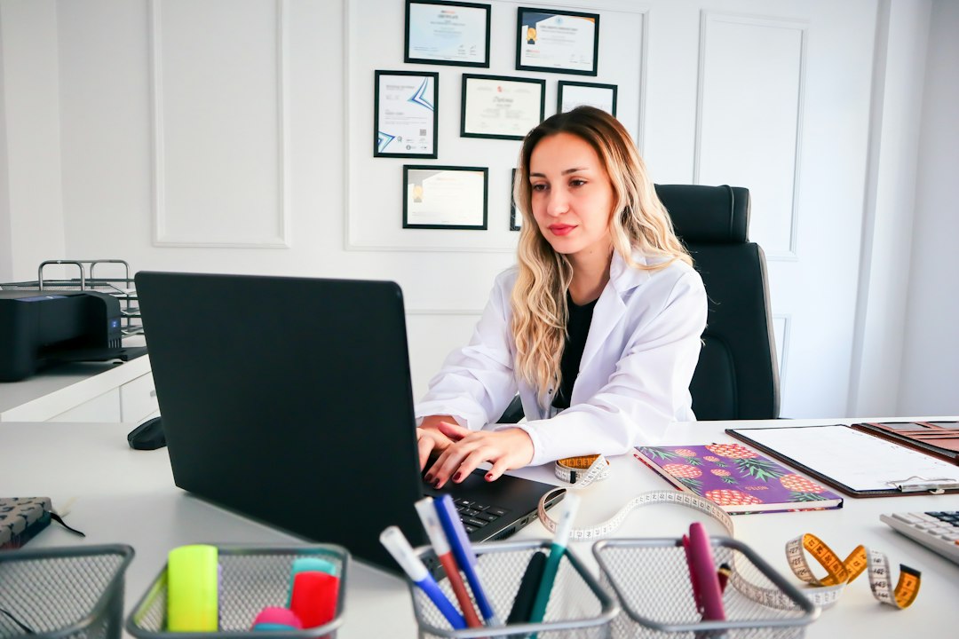 A nursing educator in a professional office reviewing licensure data on a laptop