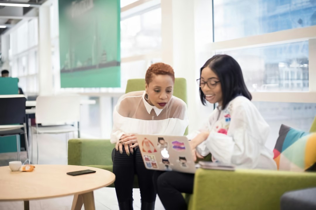 Two people review a laptop together in a bright modern learning space, one wearing a white coat