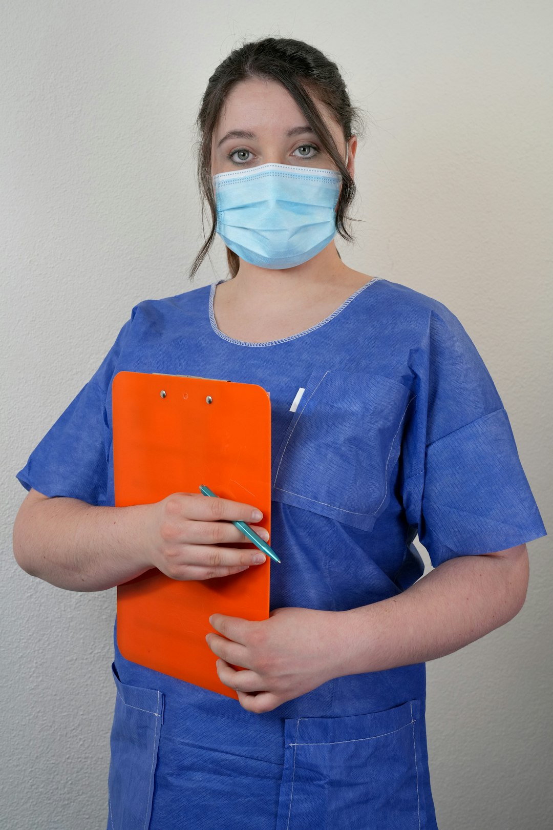 A nurse in blue scrubs holds a clipboard and pen, ready to document a clinical evaluation.