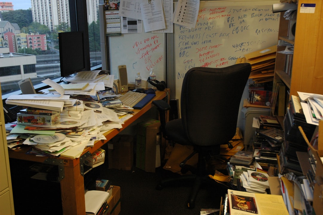 An office desk buried under overflowing papers, folders, and sticky notes